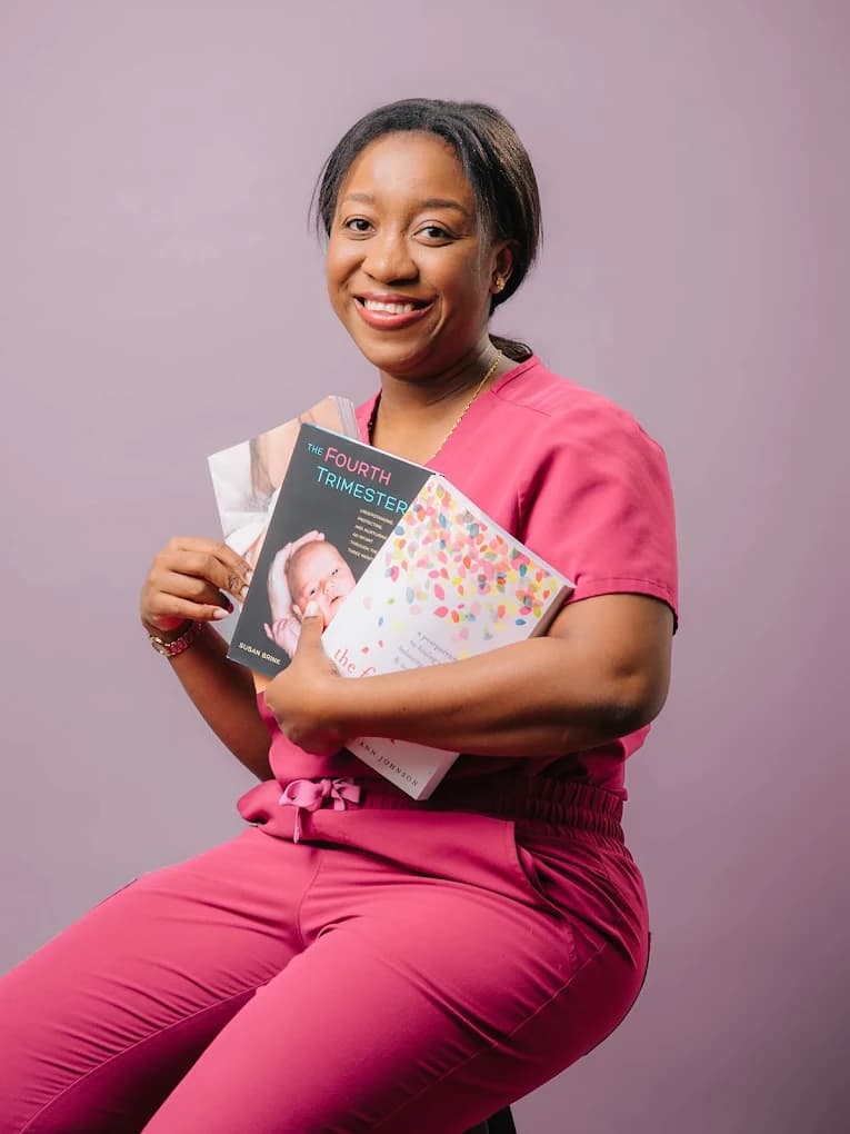 Rithalorine seated in a burgundy chair, holding the book The Fourth Trimester