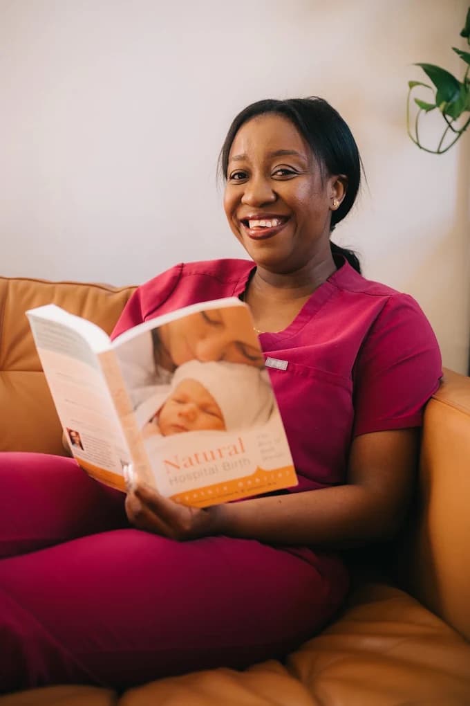 Rithalorine seated on a couch, holding the book Natural Hospital Birth